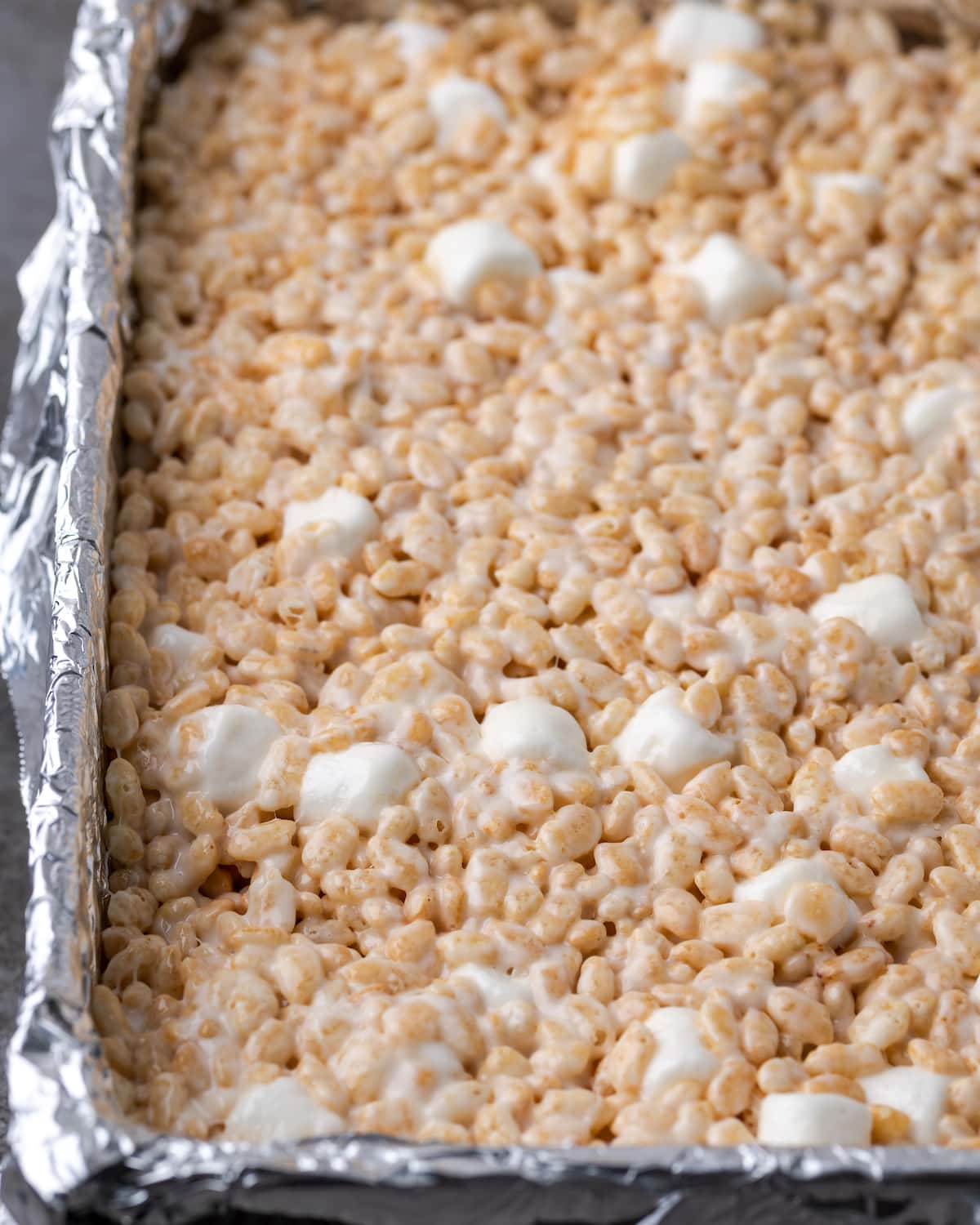 Rice Krispie treat mixture spread in a rectangular baking pan lined with foil.
