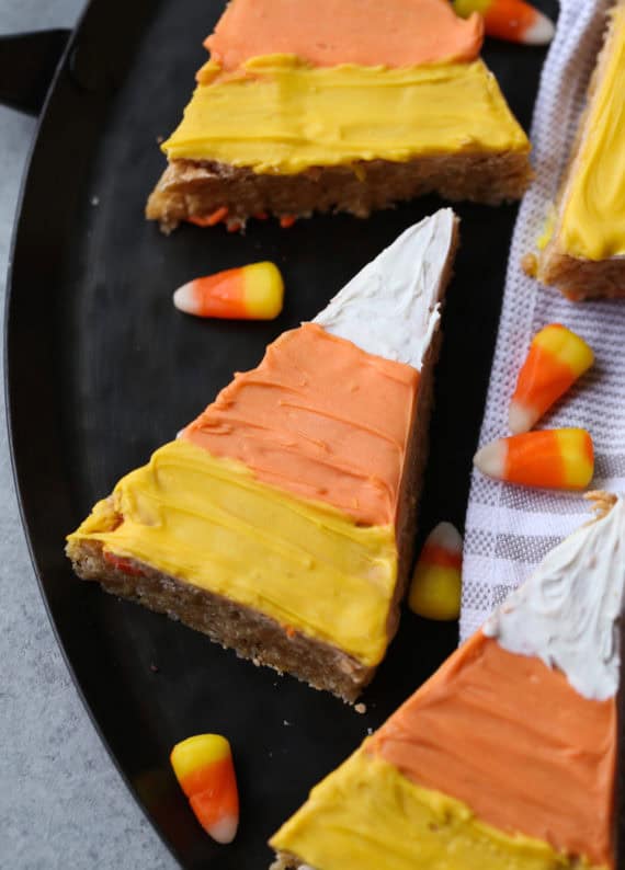 Scotcheroos shaped and decorated like candy corn on a plate next to candy corn pieces.