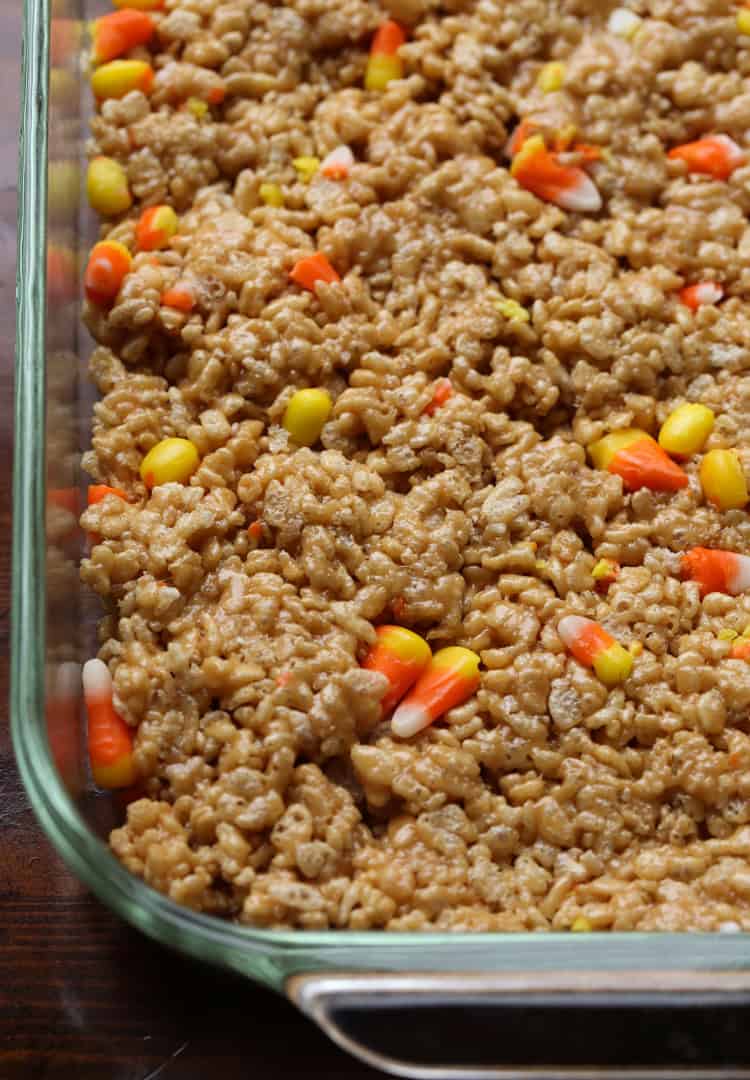 Scotcheroo peanut and crispy rice mixture with candy corn is spread into a baking dish.