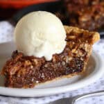 A slice of pecan pie on a white plate topped with a scoop of vanilla ice cream.