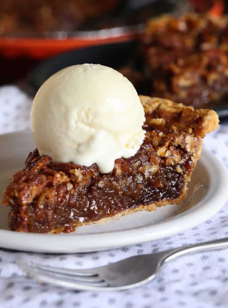 A slice of pecan pie is placed on a white plate and topped with vanilla ice cream.
