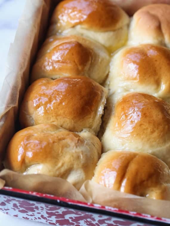 Baked dinner rolls brushed with glaze in a baking pan.