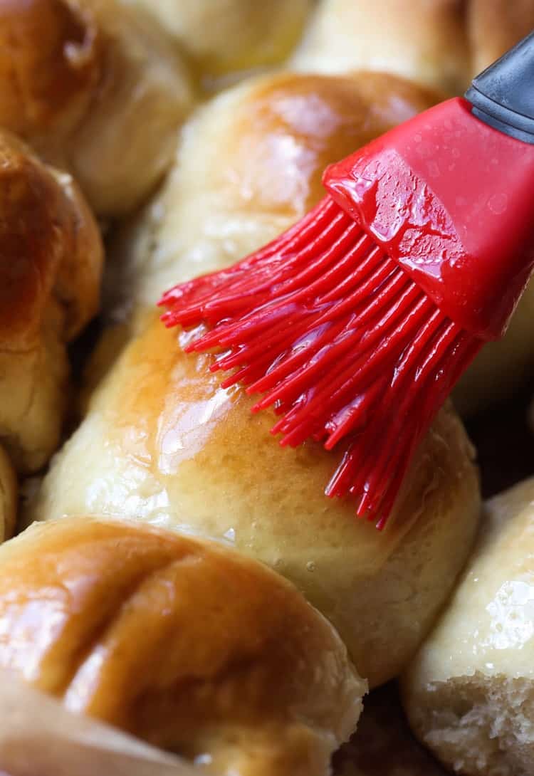 Brushing the tops of baked dinner rolls with melted honey butter.