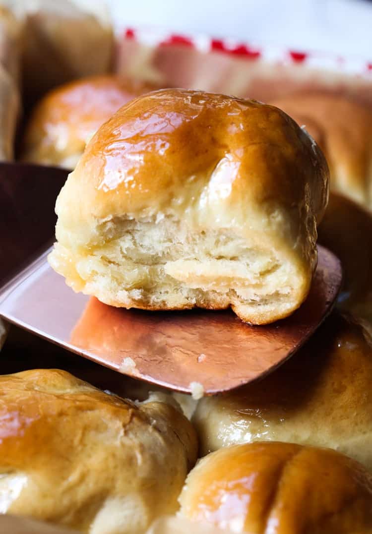 A fluffy dinner roll lifted from a baking pan with a spatula.