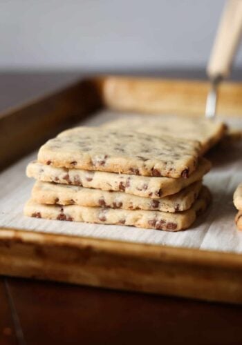 A stack of chocolate chip shortbread cookies on a lined baking sheet.
