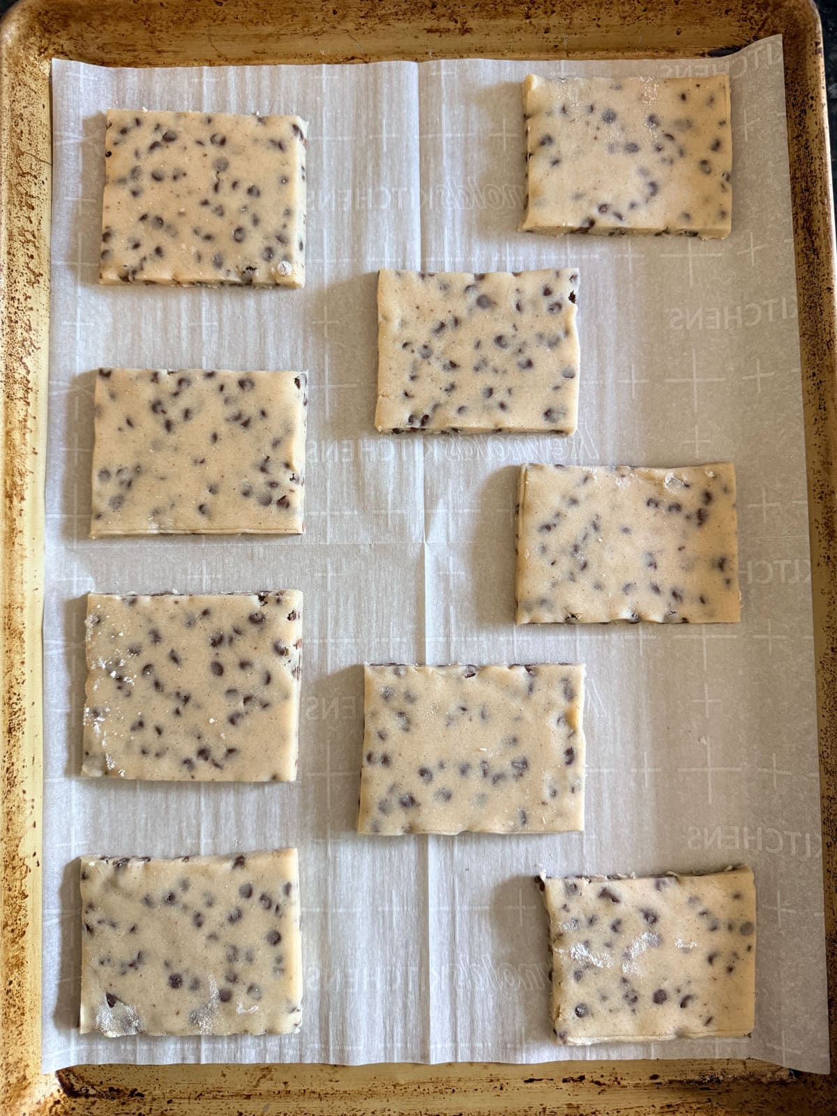 This easy chocolate chip shortbread is crisp, buttery, and loaded with mini chocolate chips. Freezer-friendly and perfect for holiday baking! Overhead view of shortbread dough cut into squares on a baking sheet.