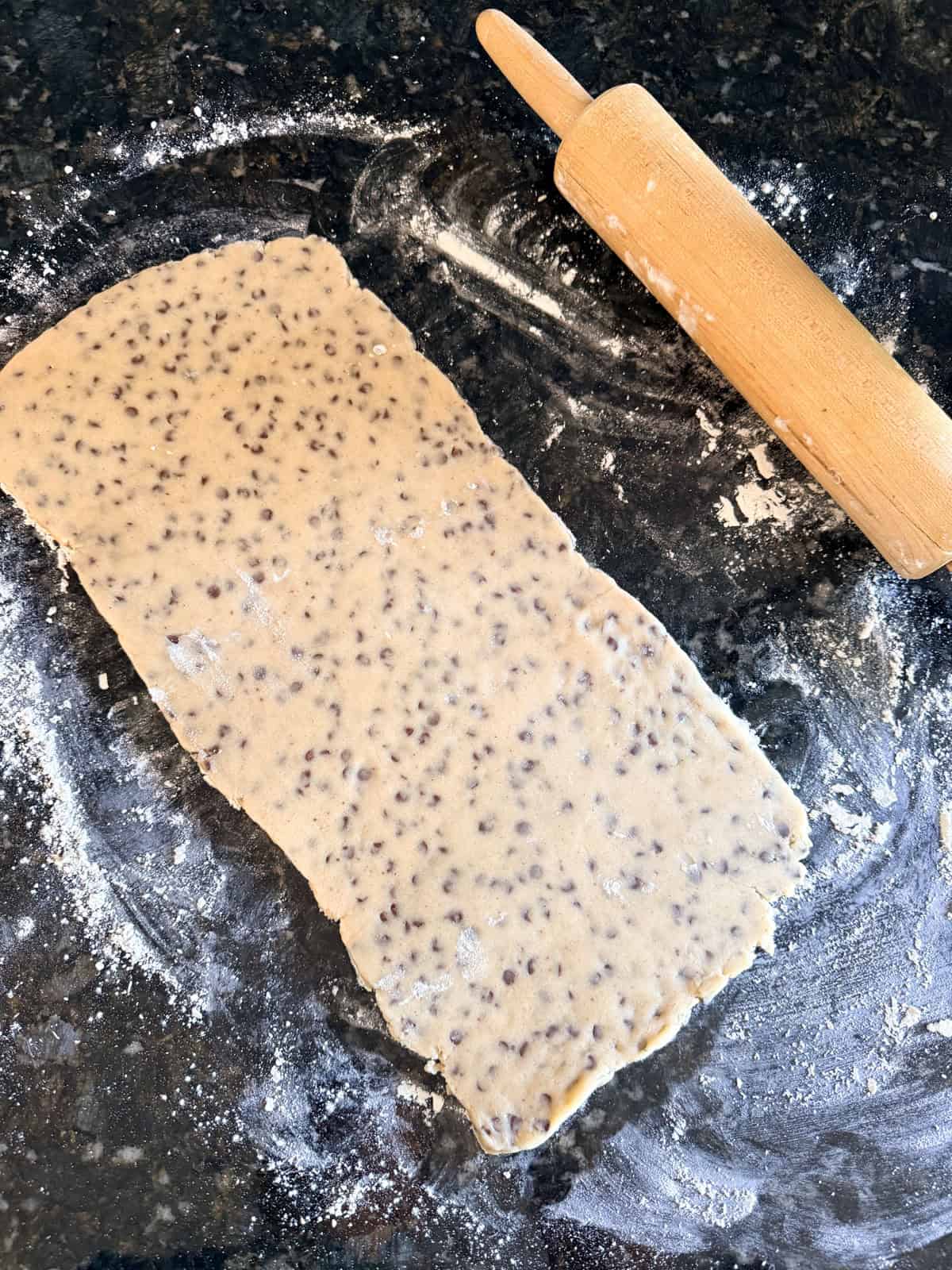 This easy chocolate chip shortbread is crisp, buttery, and loaded with mini chocolate chips. Freezer-friendly and perfect for holiday baking! Chocolate chip shortbread dough rolled out on a floured countertop.