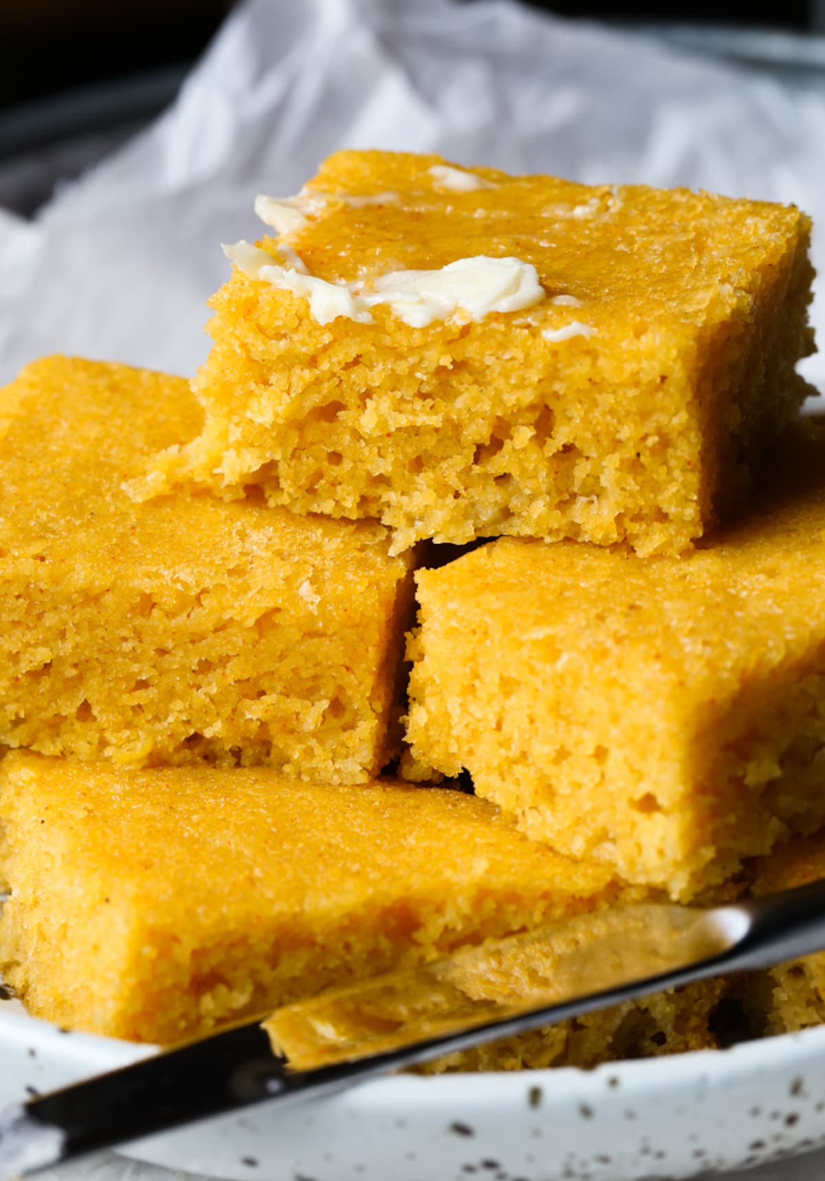 A stack of cut cornbread on a plate topped with butter
