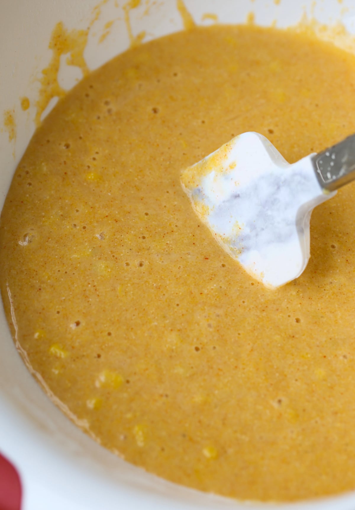 Mixing corn bread batter in a white bowl with a rubber spatula