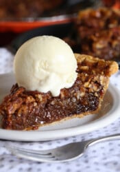 A slice of pecan pie on a white plate with a scoop of ice cream