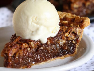 A slice of pecan pie on a white plate with a scoop of ice cream