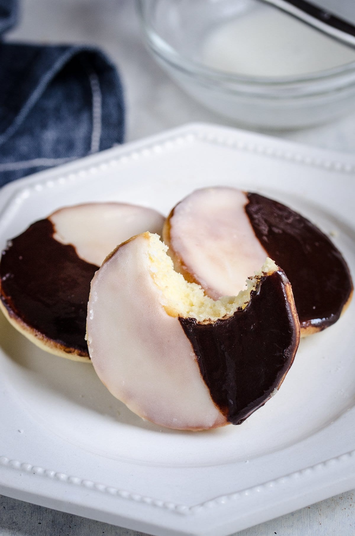Black and white cookies on a plate, one with a bite missing.