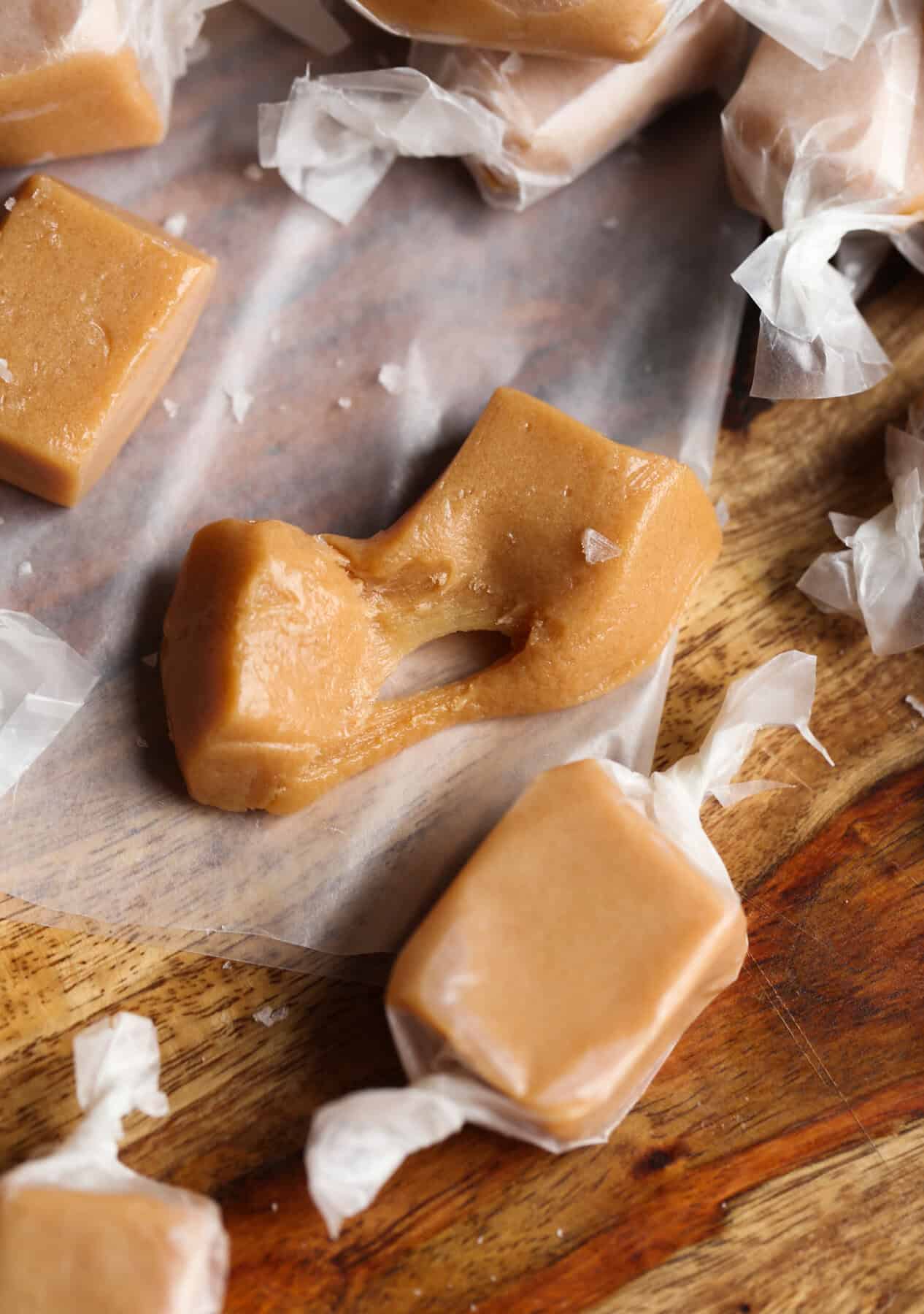 Close up view of a caramel piece that's been pulled apart, surrounded by wrapped caramels.