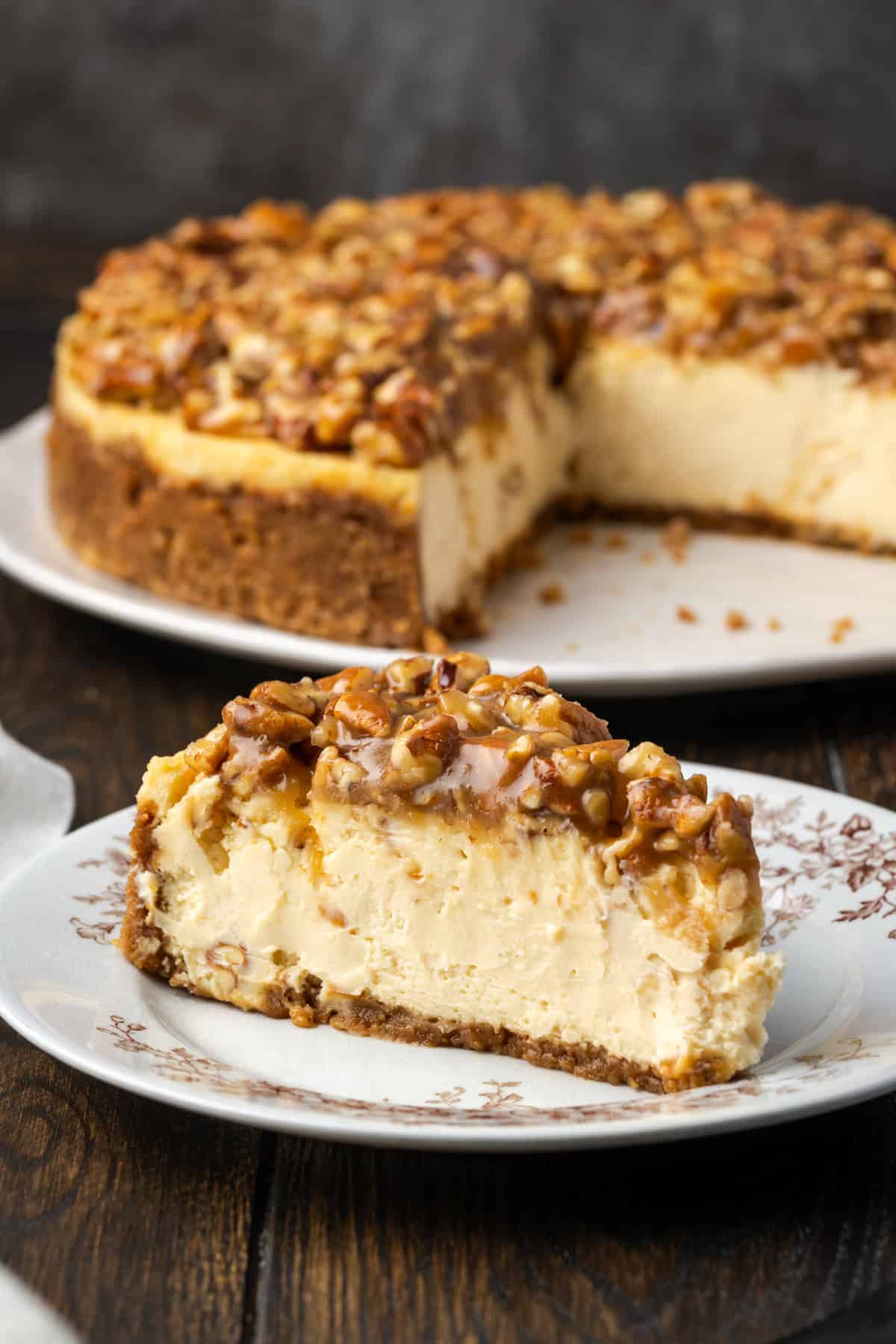 A slices of pecan pie cheesecake on a plate with the rest of the cheesecake in the background.