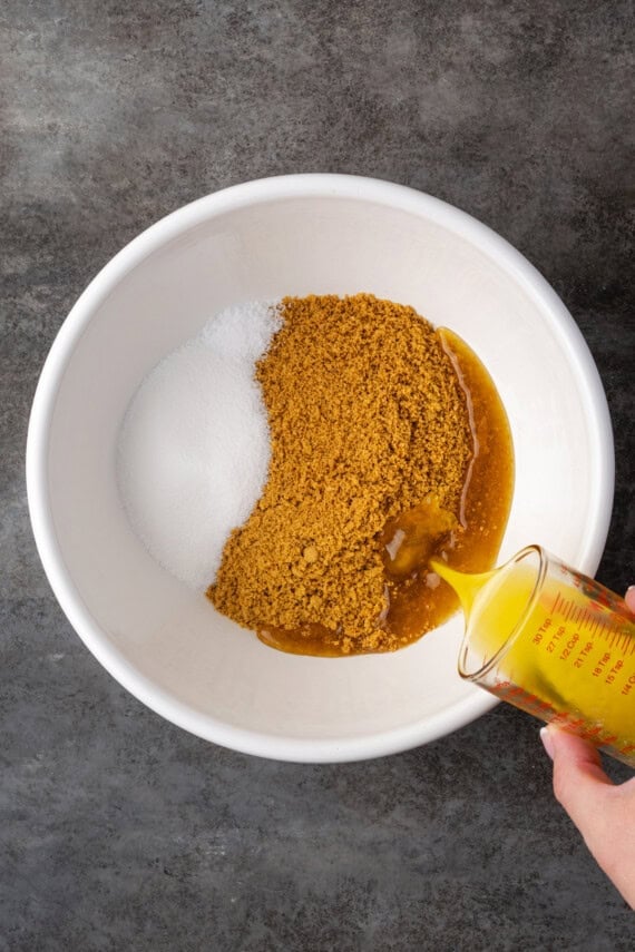 Overhead view of melted butter being added to a bowl of sugar and graham cracker crumbs.