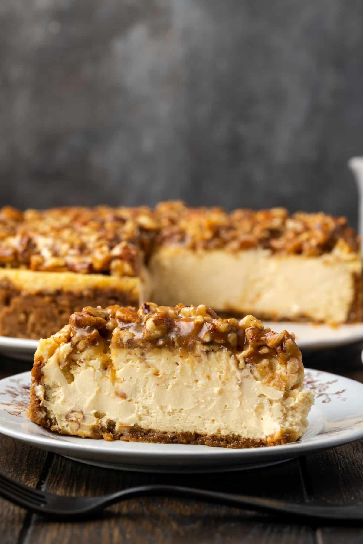 A slice of pecan pie cheesecake on a China plate with the rest of the cheesecake in the background.