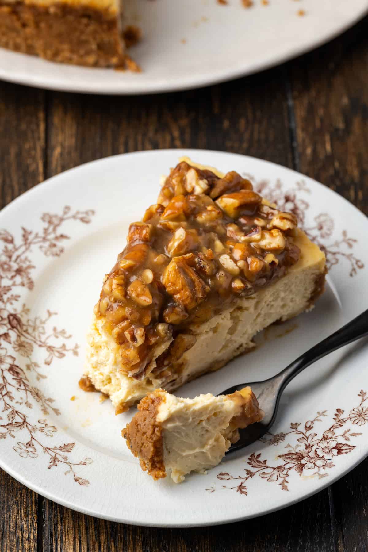 A slice of pecan pie cheesecake with a forkful resting beside it on a decorative China plate.