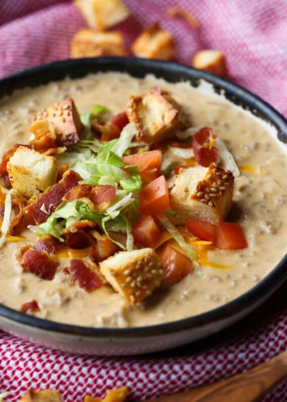 A bowl of cheeseburger soup garnished with diced tomatoes, shredded lettuce, bacon, and croutons.