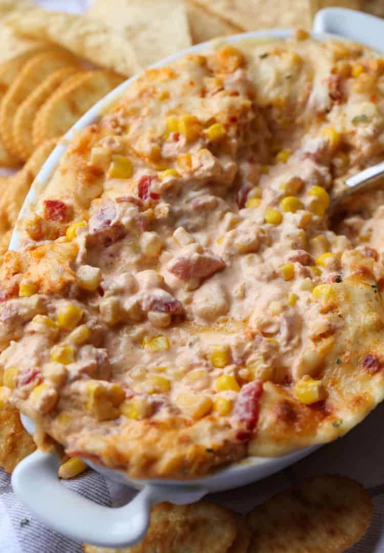 Hot corn dip in an oval baking dish served next to assorted crackers.