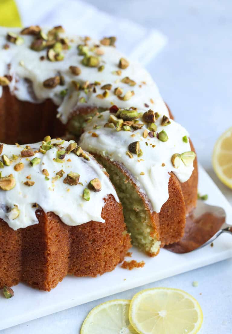 Frosted pistachio lemon cake decorated with crushed pistachios on a square plate.