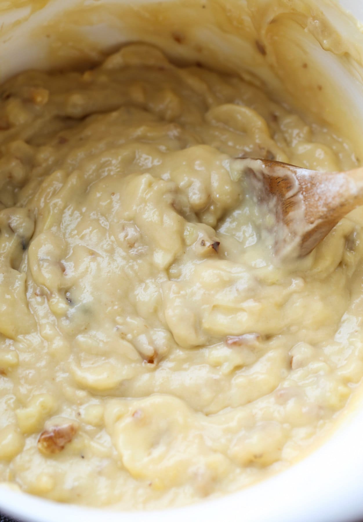 Banana muffin dough in a white bowl being stirred with a wooden spoon.