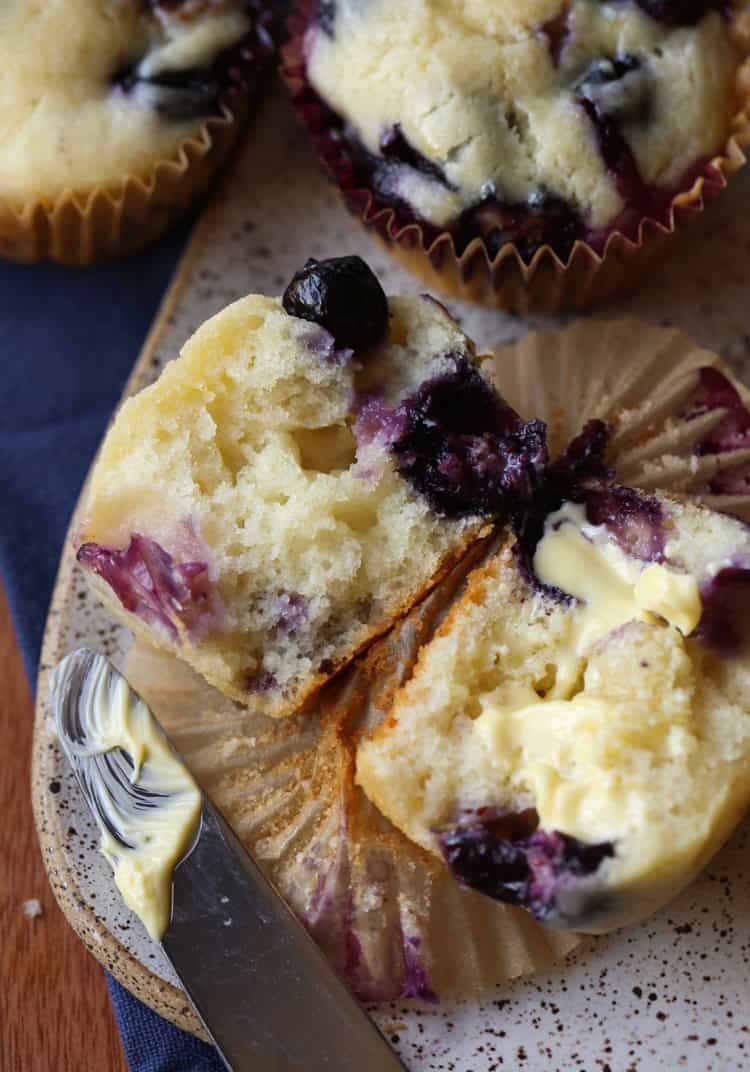 Two halves of a fluffy blueberry muffin buttered on a plate.