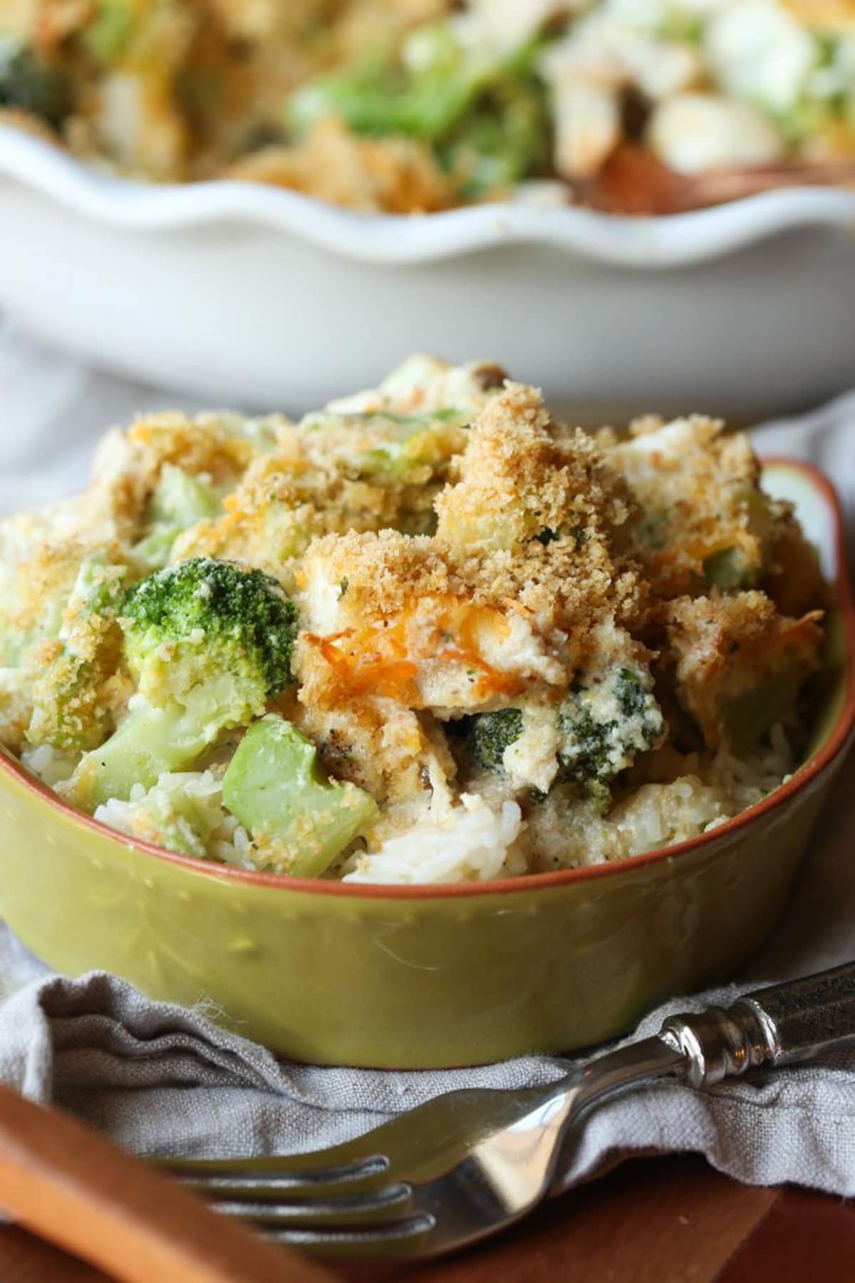 Close up of chicken divan served in a green stoneware bowl with the rest of the casserole in the background.