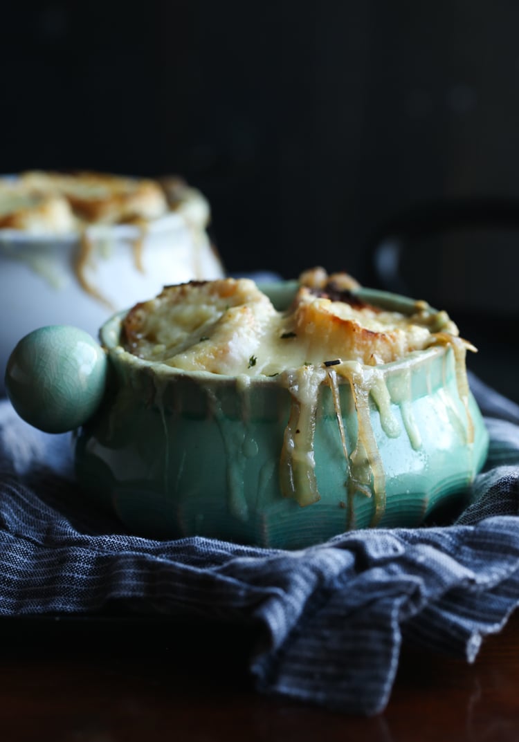 A ramekin full of French onion soup, topped with bread slices and melted Gruyere cheese.