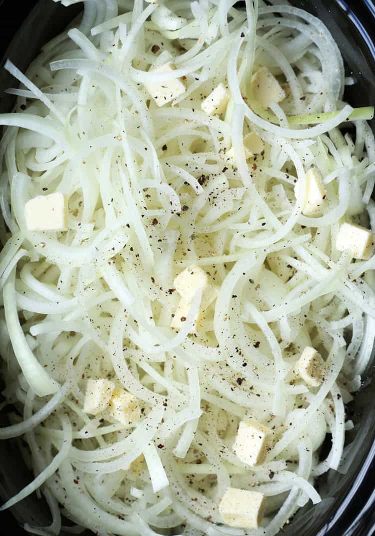 Chopped yellow onions combined with butter in the bowl of a slow cooker.