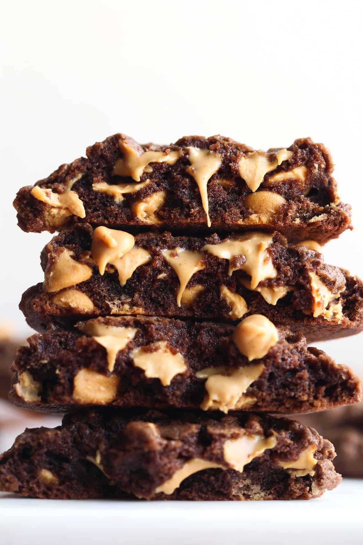 Stacked chocolate cookies broken in half showing melty peanut butter chips on the inside. 