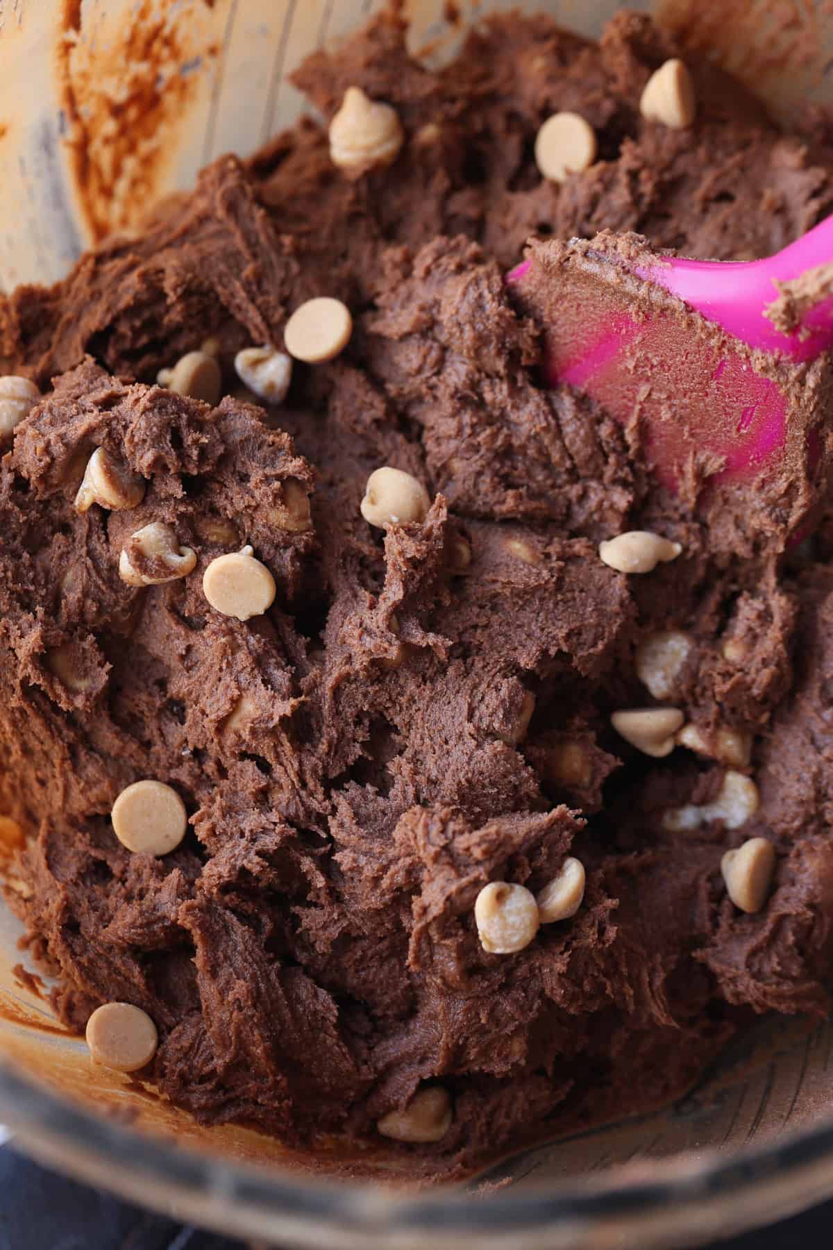 Chocolate cookie dough with peanut butter chips in a mixing bowl with a pink rubber spatula