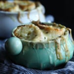 A ramekin full of French onion soup, topped with bread slices and melted Gruyere cheese.