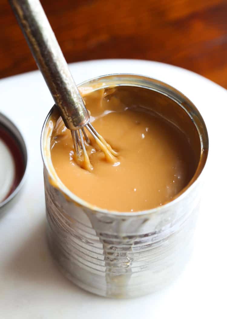 Overhead view of an open can of dulce de leche with a whisk.