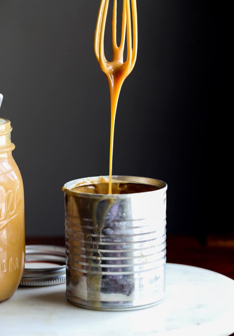 A whisk drizzling dulce de leche into a can.