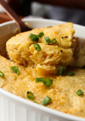 A spoon scoops a serving of cornbread chicken casserole from a baking dish.