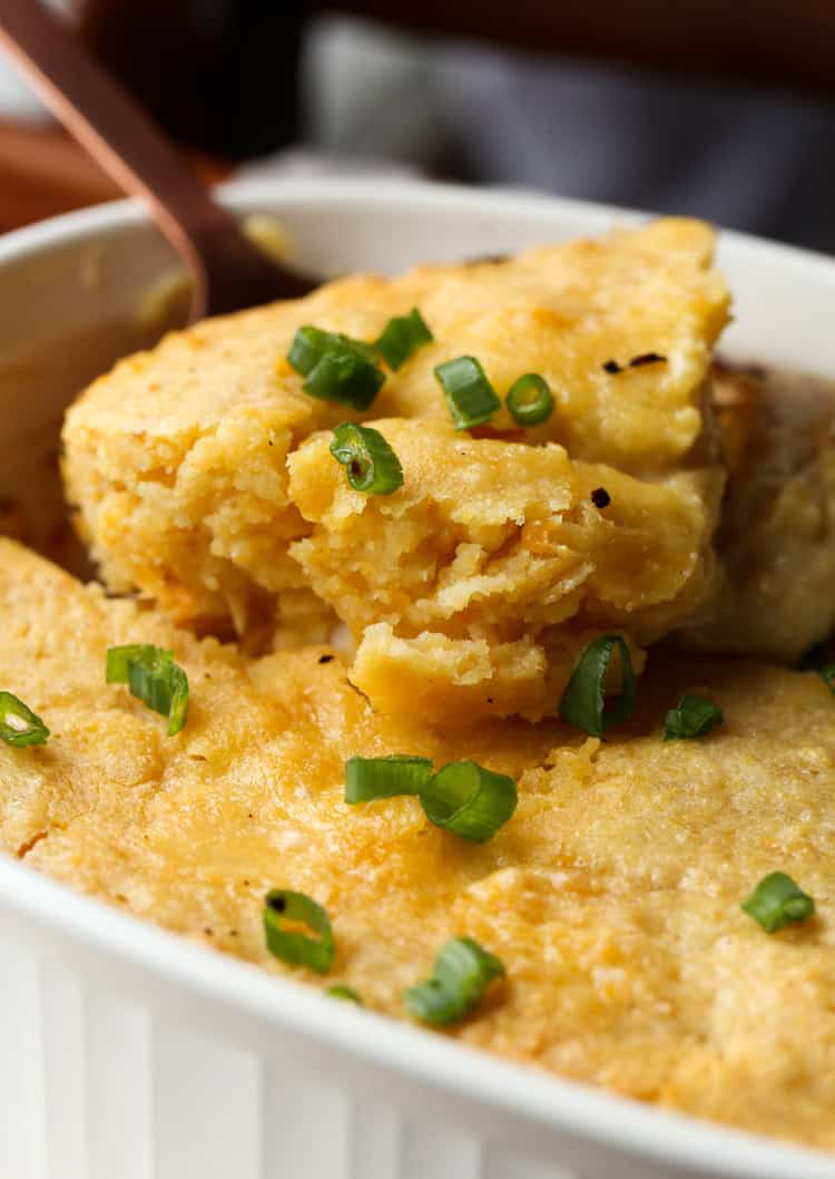 A spoon scoops a serving of cornbread chicken casserole from a baking dish.