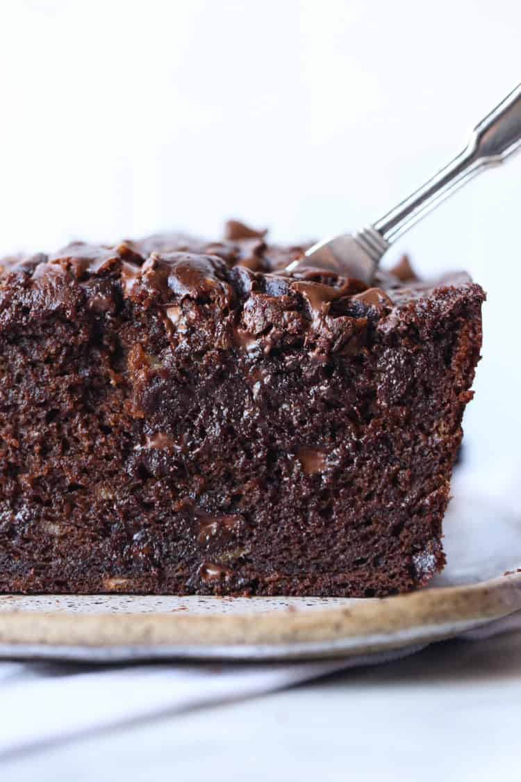 Front view of a knife slicing into a loaf of chocolate banana bread on a cutting board.