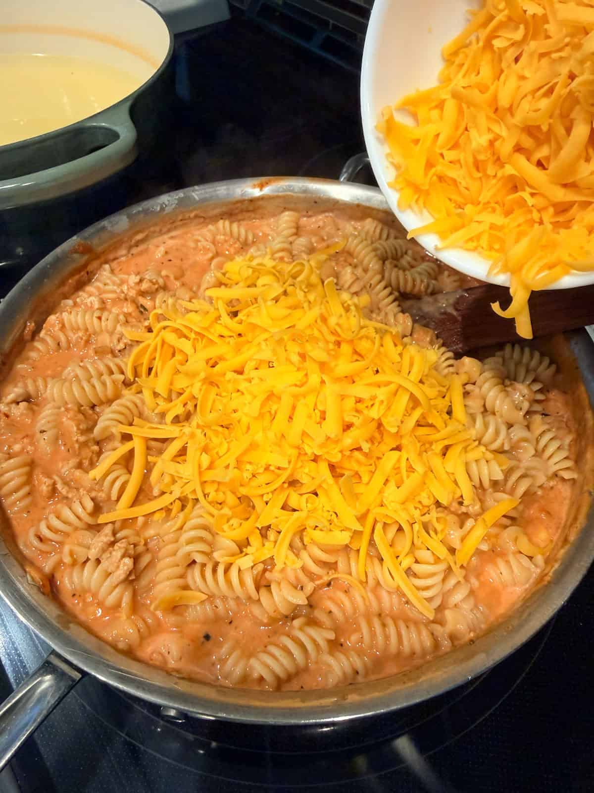 This easy beef pasta recipe is a one-pan dinner made in 30 minutes! Packed with juicy ground beef, cheese, and pasta in creamy tomato sauce. Shredded cheese added to creamy beef pasta in a skillet.