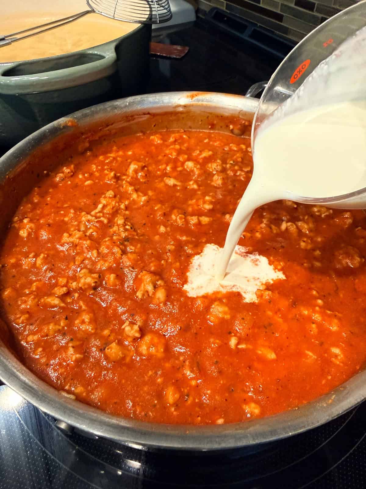 This easy beef pasta recipe is a one-pan dinner made in 30 minutes! Packed with juicy ground beef, cheese, and pasta in creamy tomato sauce. Pouring cream into meat sauce in a skillet.