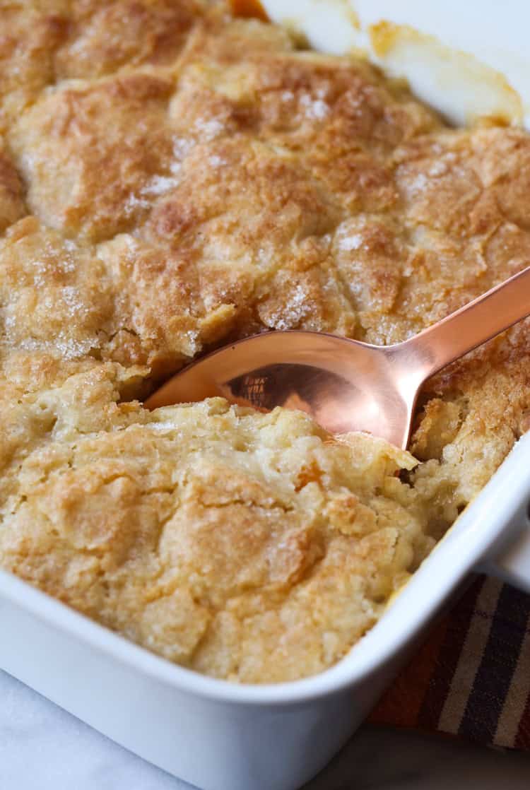 A spoon is used to scoop peach cobbler from a baking dish.