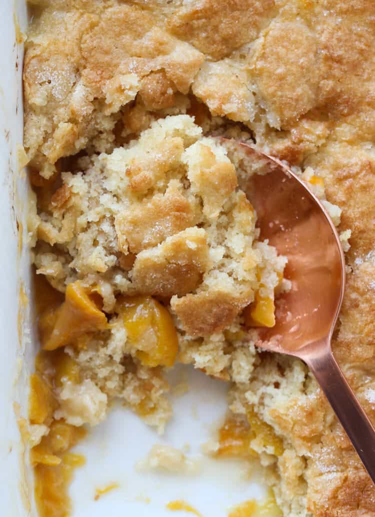 A spoon is used to scoop peach cobbler from a baking dish.