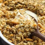 A serving spoon scoops into a poppyseed chicken casserole in a baking dish.