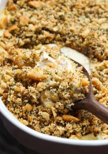 A serving spoon scoops into a poppyseed chicken casserole in a baking dish.
