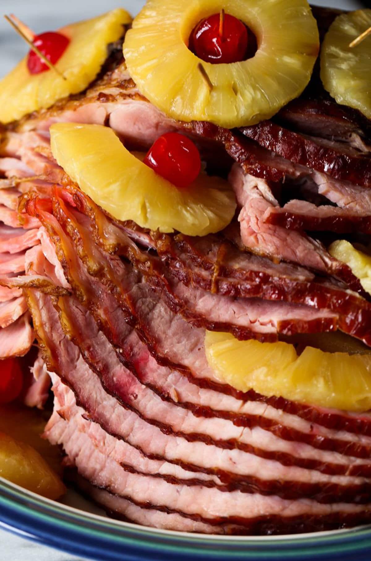 The moist heat of an oven bag is the secret to perfect baked ham! This easy baked ham recipe is juicy and tender with the best sweet glaze. Baked ham with pineapple and cherries on a serving platter, drizzled with brown sugar glaze.