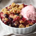 Mixed Berry Crisp in a white dish topped with a scoop of strawberry ice cream.