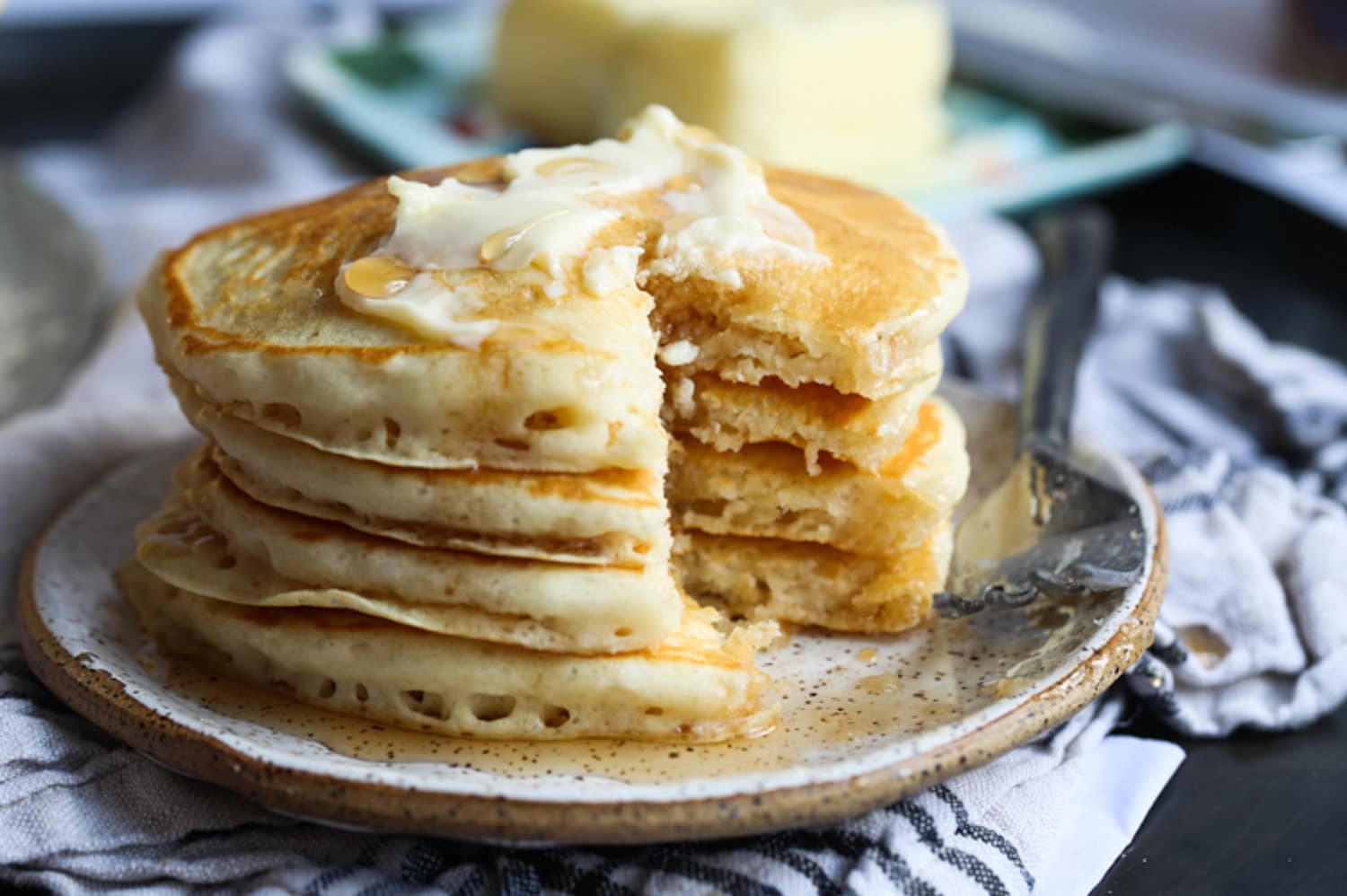 Stacked pancakes on a plate with butter and a slice missing