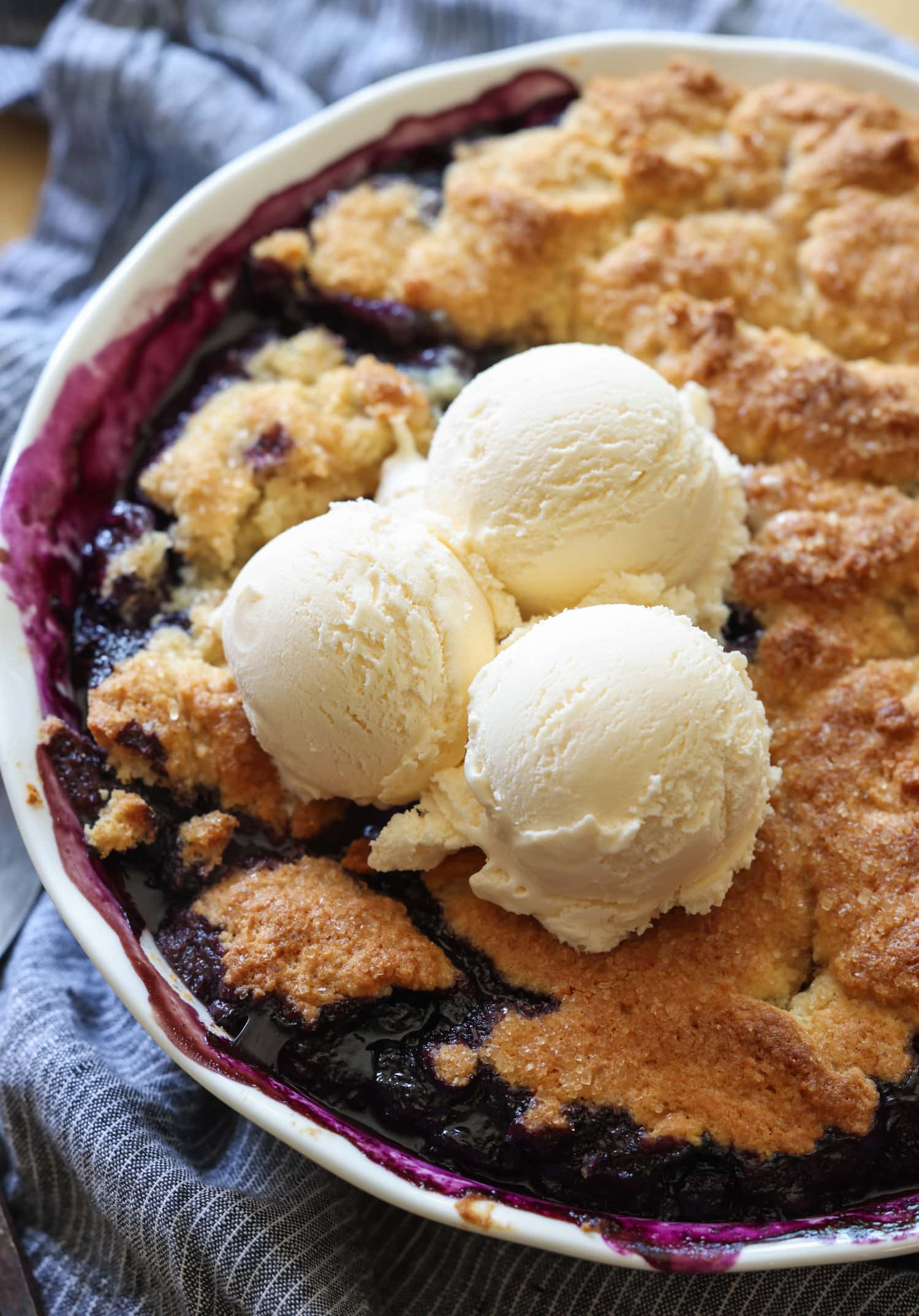 Blueberry cobbler in a pie plate with 3 scoops of vanilla ice cream on top