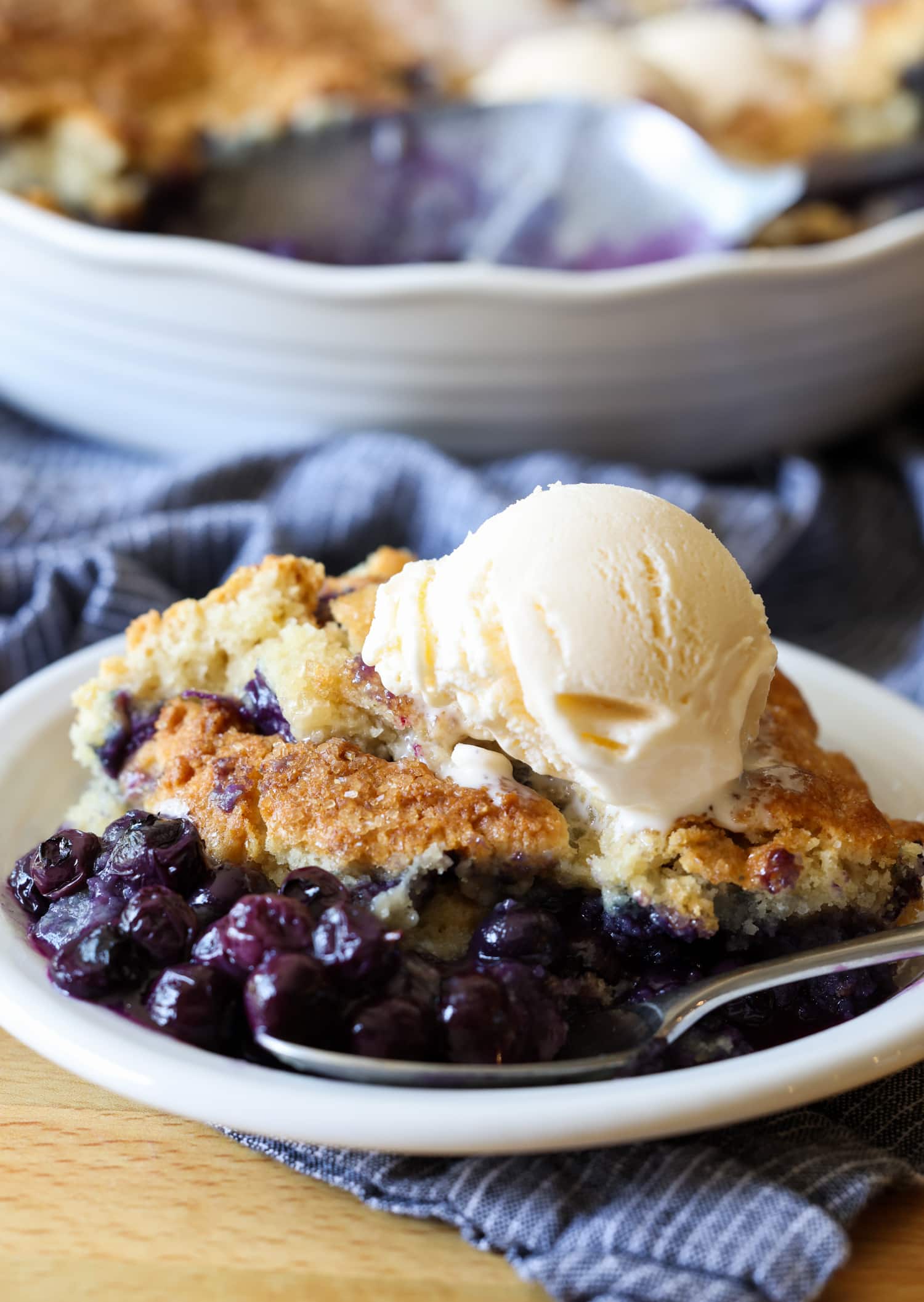 A scoop of blueberry cobbler on a white plate with vanilla ice cream on top
