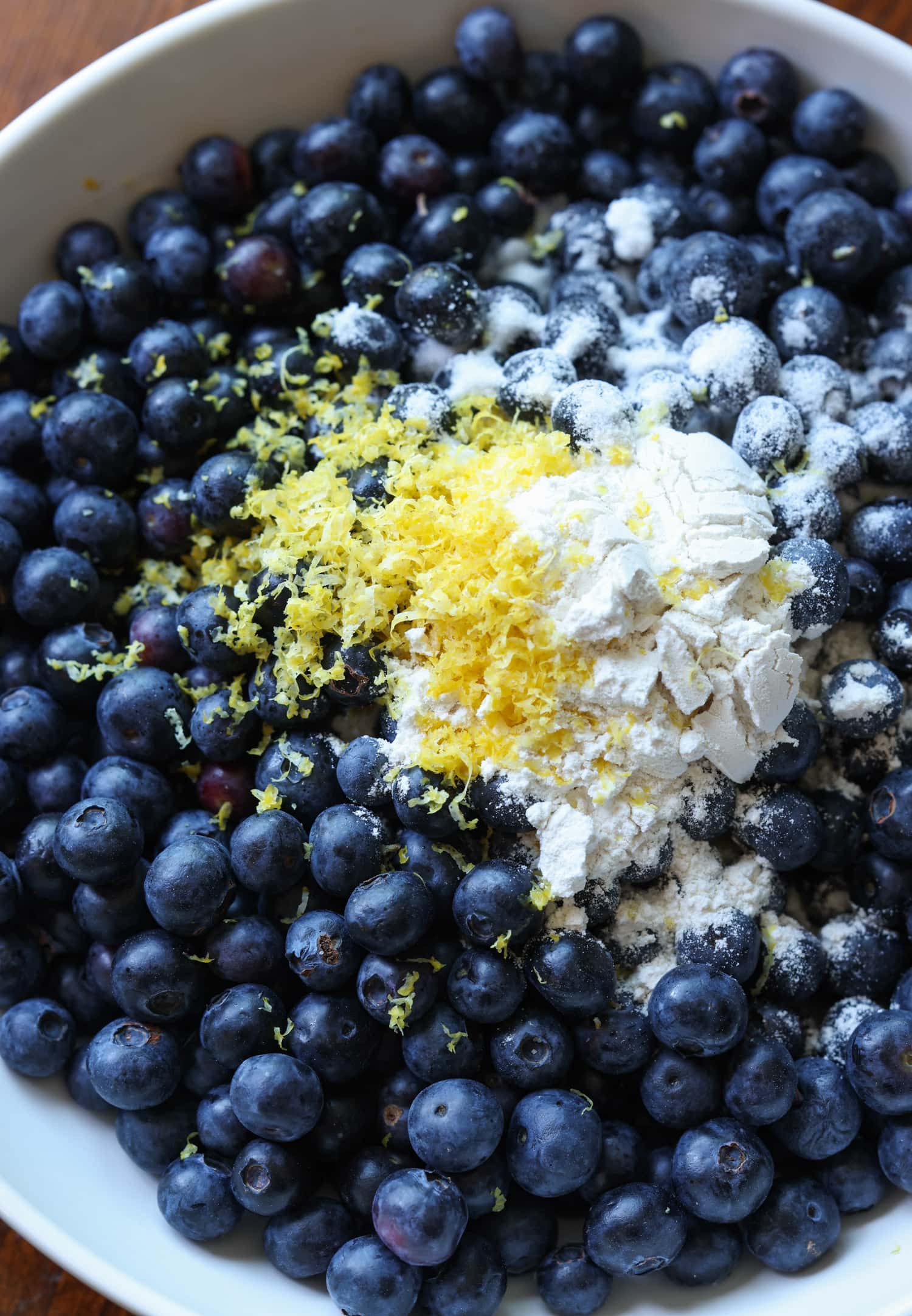 Blueberries, flour, and lemon zest in a white bowl