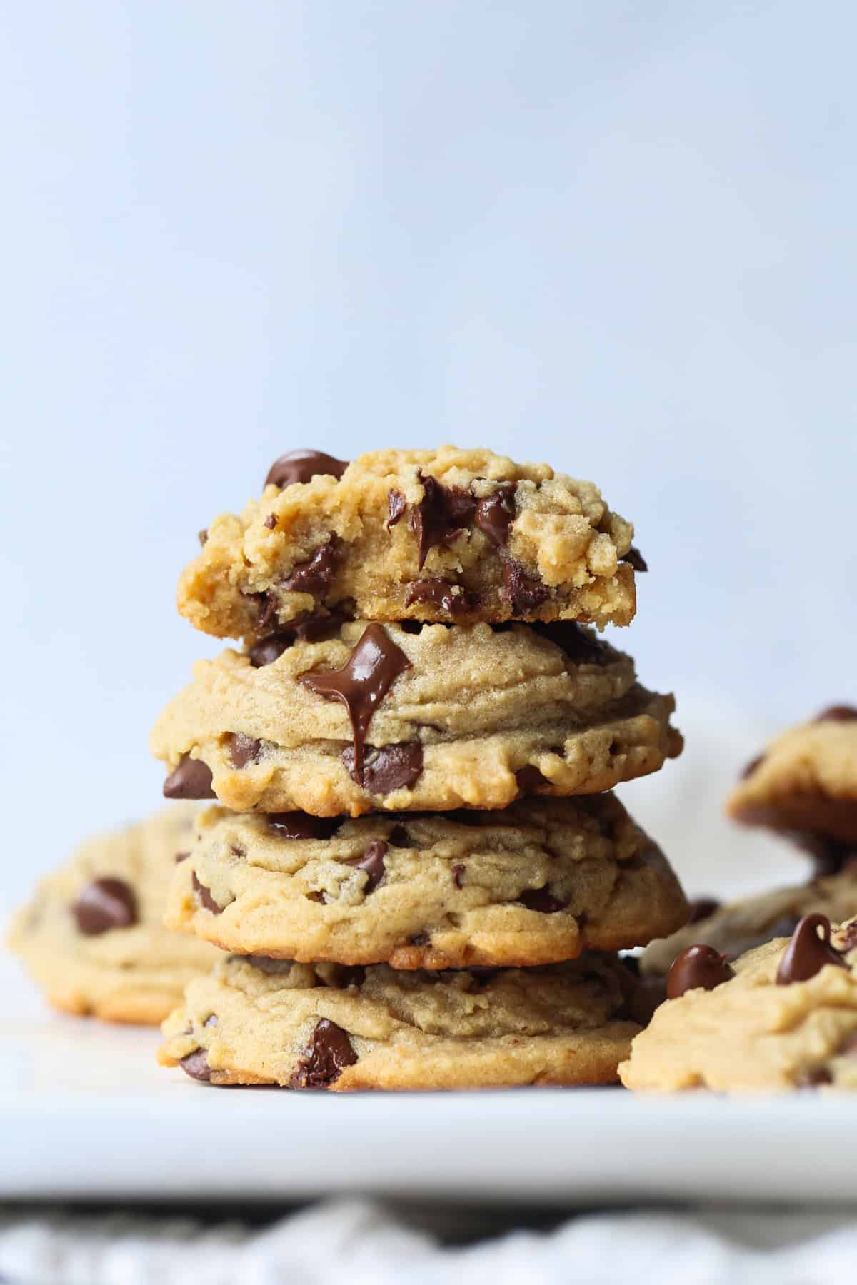 Four thick peanut butter cookies with chocolate chips stacked on a white ceramic plate.